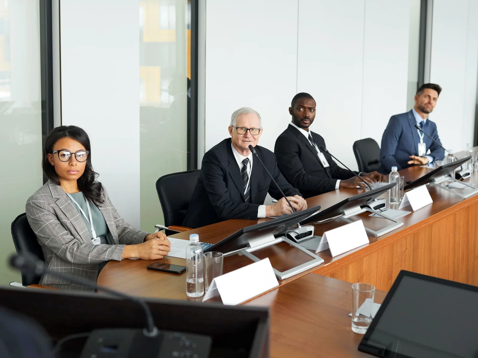 Four people seated at a long meeting table with microphones and name cards
