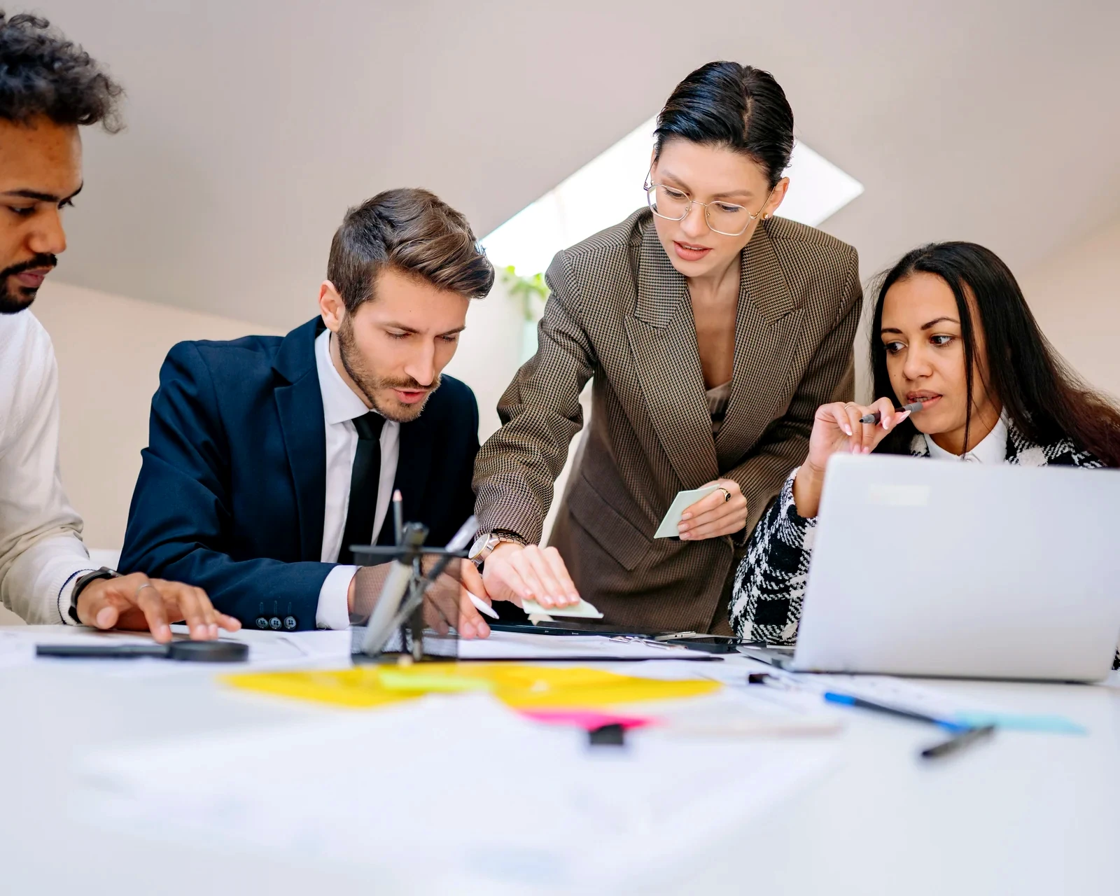 Four colleagues working together over documents and a laptop at a shared desk